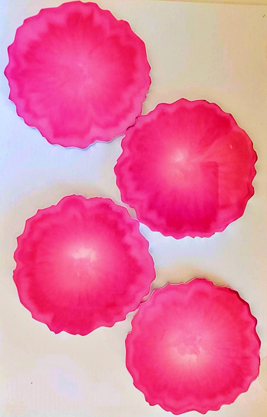 A set of four pink geode-style resin coasters with silver edges on a white background.