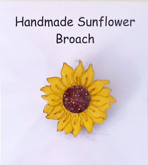 A handmade sunflower brooch with vibrant yellow leaves and a sparkly brown center, displayed on a white background.
