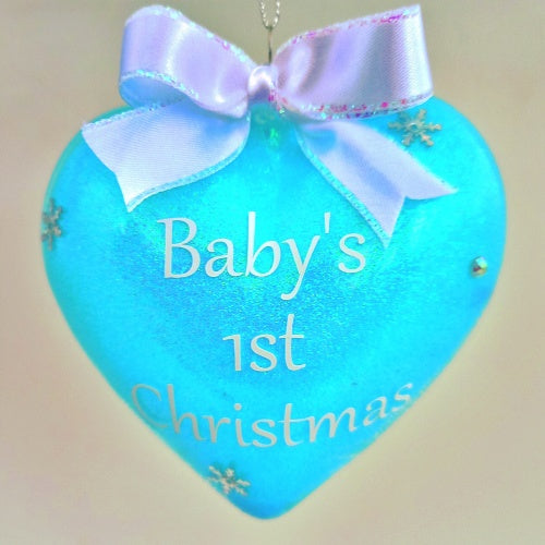 A blue heart-shaped Christmas bauble with 'Baby's 1st Christmas' written on it, adorned with a white ribbon bow at the top.