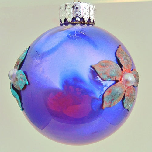 A round blue Christmas bauble with decorative elements, hanging on a tree.