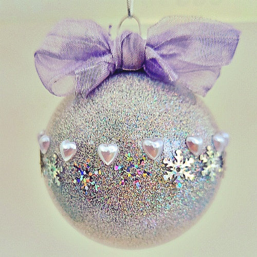 A silver Christmas bauble with a blue bow, decorated with white hearts and glittering snowflakes.