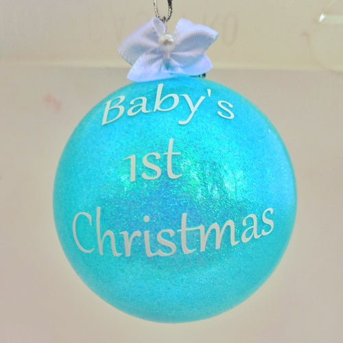 A blue round Christmas bauble with the phrase 'Baby's 1st Christmas' written on it, adorned with a pretty white bow at the top.