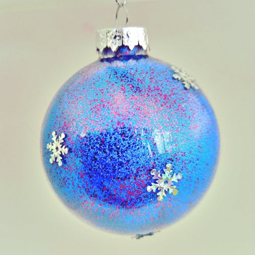 A round blue Christmas bauble decorated with white snowflakes and glitter.