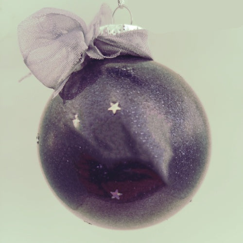 A round purple Christmas bauble decorated with white stars and topped with a grey bow.