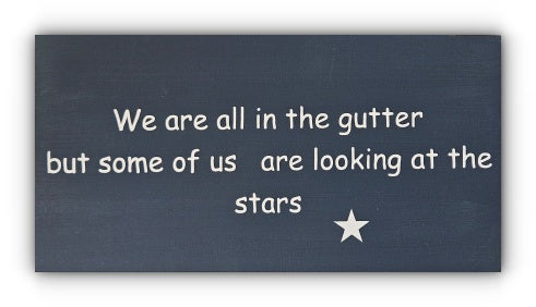 A handmade wooden plaque with a quote that reads 'We are all in the gutter but some of us are looking at the stars' in white vinyl lettering, accompanied by a small star symbol.