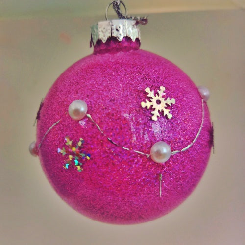 A round lilac Christmas bauble decorated with silver snowflakes and faux pearls, hanging on a tree.